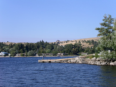 [A dock sticking out into the water from a small hillside. Plenty of trees around the edge of the water with some somewhat barren hillside above and behind them.]